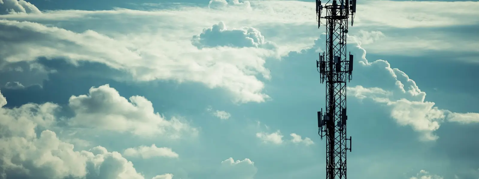 A telecommunications mast carrying sector antennas, standing against a bank of cloud.